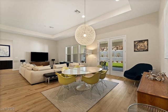 dining room with a tray ceiling, light hardwood / wood-style floors, and french doors