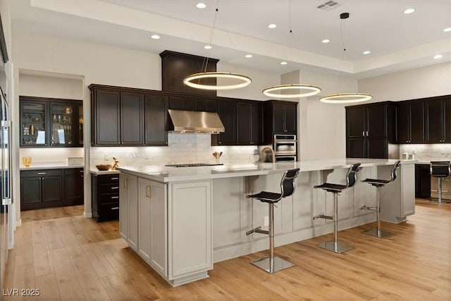 kitchen with black gas cooktop, decorative light fixtures, a tray ceiling, a large island, and light hardwood / wood-style floors