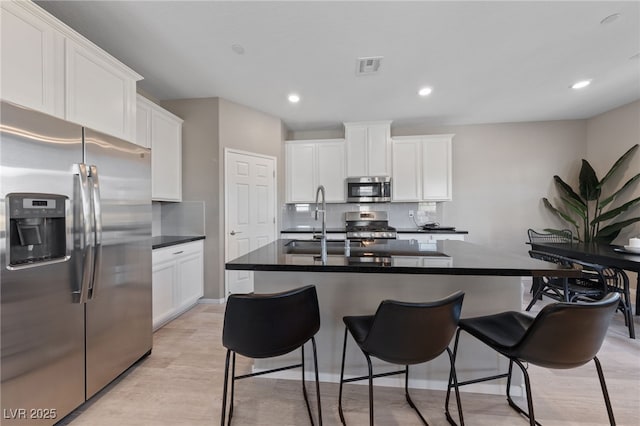 kitchen with appliances with stainless steel finishes, a center island with sink, and white cabinets