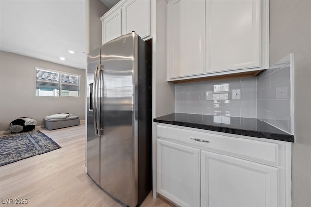 kitchen with dark stone countertops, white cabinets, backsplash, light hardwood / wood-style floors, and stainless steel refrigerator with ice dispenser