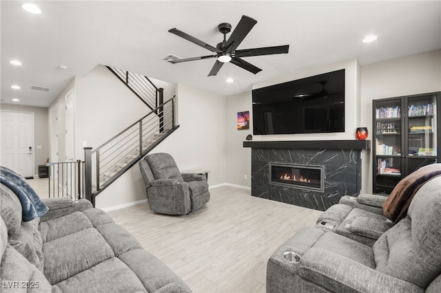 living room featuring a high end fireplace, ceiling fan, and light wood-type flooring