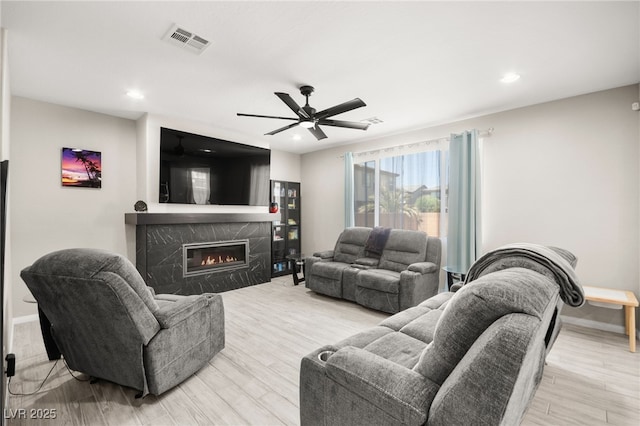 living room featuring light hardwood / wood-style floors, a premium fireplace, and ceiling fan