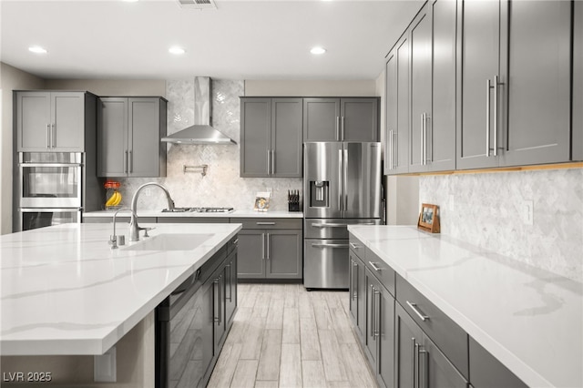 kitchen with appliances with stainless steel finishes, sink, gray cabinetry, light stone countertops, and wall chimney range hood