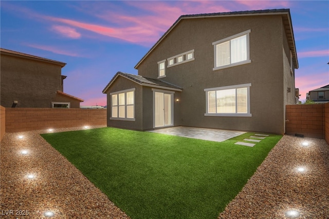 back house at dusk featuring a yard and a patio area