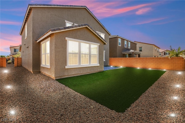 back house at dusk featuring a lawn