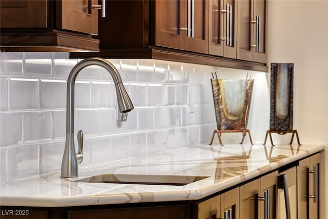 room details with light stone counters, sink, and backsplash