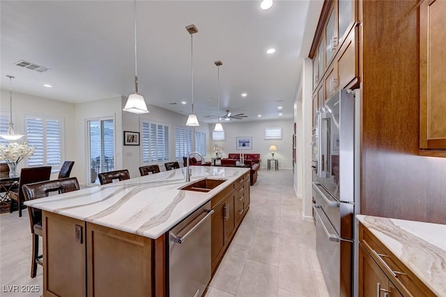 kitchen featuring light stone counters, hanging light fixtures, a kitchen breakfast bar, an island with sink, and stainless steel appliances