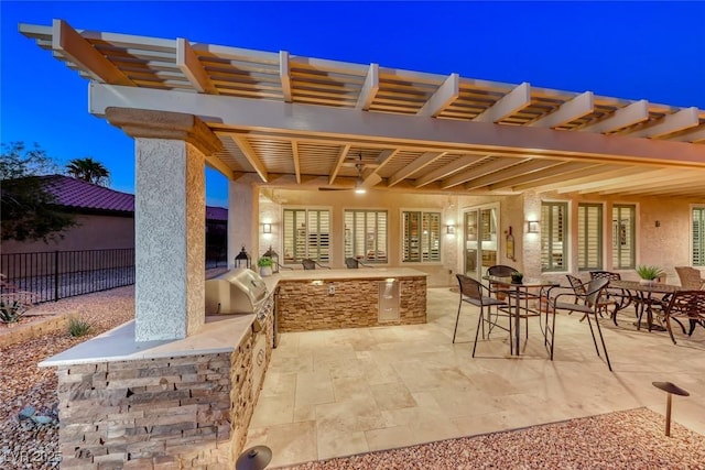 patio terrace at dusk featuring an outdoor kitchen and a grill