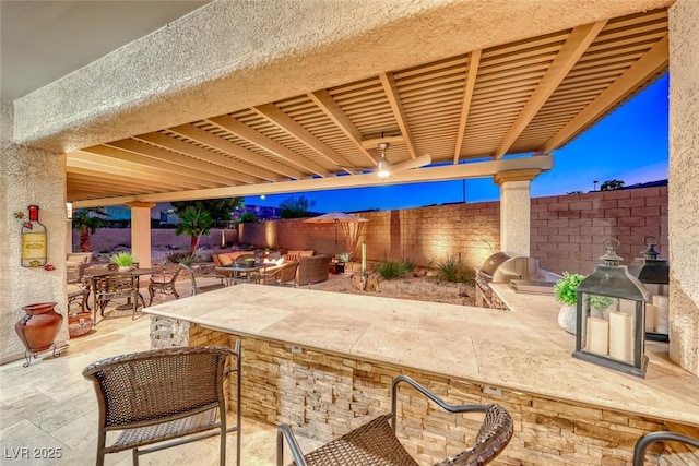 patio terrace at dusk with exterior kitchen and a pergola