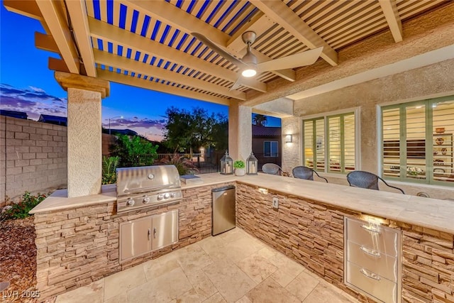 patio terrace at dusk with area for grilling, a pergola, ceiling fan, and exterior kitchen