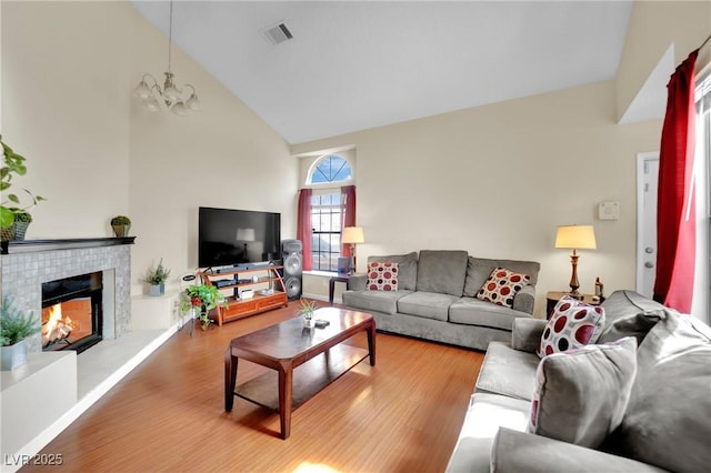 living room featuring visible vents, an inviting chandelier, wood finished floors, high vaulted ceiling, and a tile fireplace