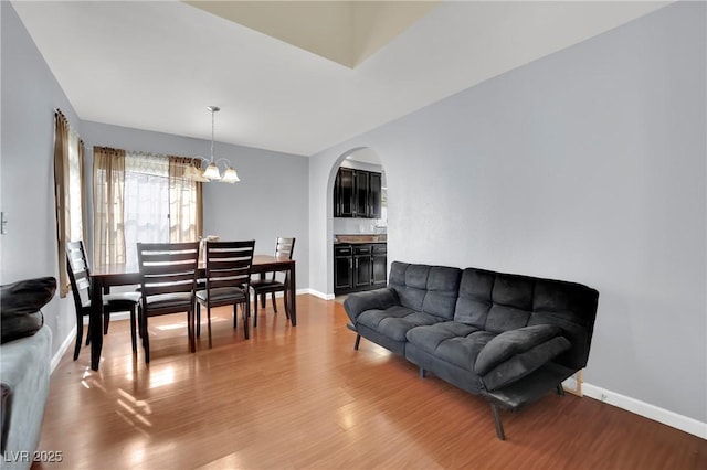 living room with an inviting chandelier, baseboards, arched walkways, and wood finished floors