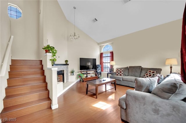 living area featuring visible vents, a fireplace with raised hearth, stairway, wood finished floors, and high vaulted ceiling