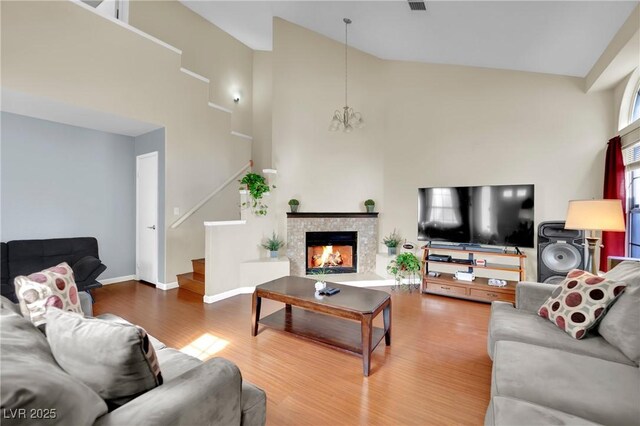 living area with a warm lit fireplace, a notable chandelier, wood finished floors, baseboards, and stairway