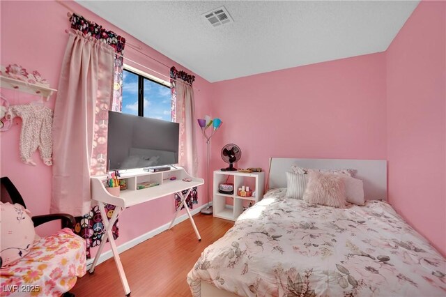 bedroom with visible vents, a textured ceiling, baseboards, and wood finished floors