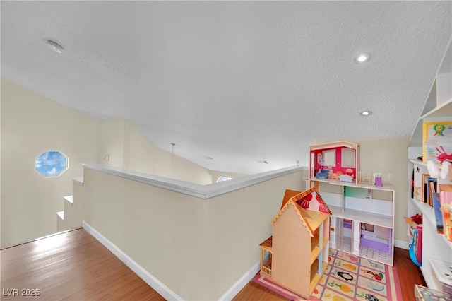 recreation room with a textured ceiling, vaulted ceiling, and wood finished floors