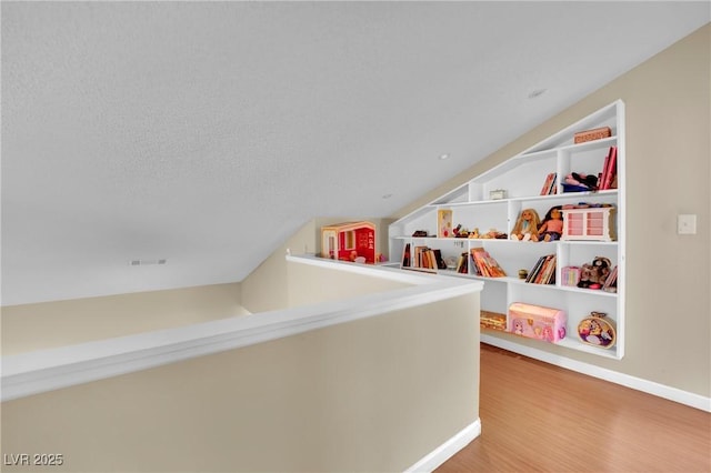 rec room featuring lofted ceiling, a textured ceiling, wood finished floors, and baseboards