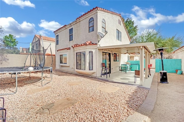 back of property featuring a trampoline, a patio, stucco siding, fence, and a tiled roof