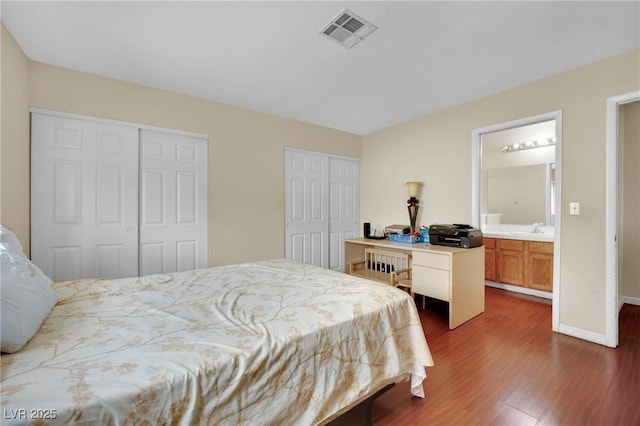 bedroom featuring baseboards, visible vents, dark wood finished floors, multiple closets, and a sink