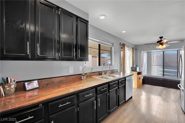 kitchen featuring a sink, light wood finished floors, appliances with stainless steel finishes, and dark cabinets