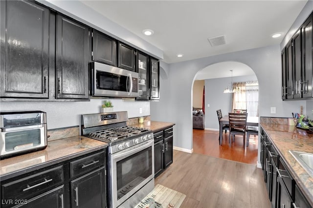 kitchen featuring arched walkways, dark cabinets, visible vents, appliances with stainless steel finishes, and light wood finished floors