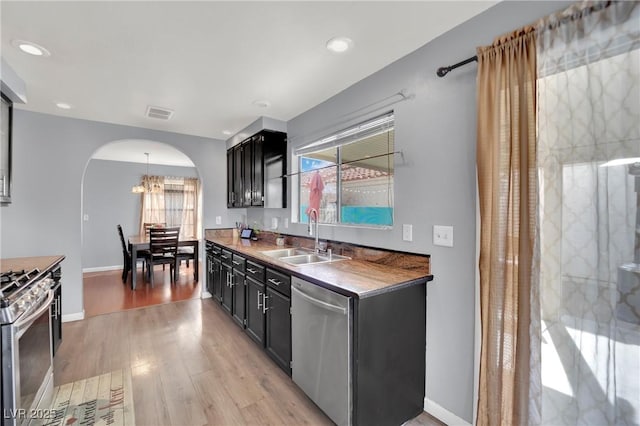 kitchen featuring arched walkways, appliances with stainless steel finishes, light wood-style floors, a sink, and dark cabinets