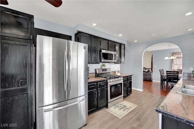 kitchen with arched walkways, stainless steel appliances, recessed lighting, light wood-style flooring, and dark cabinetry