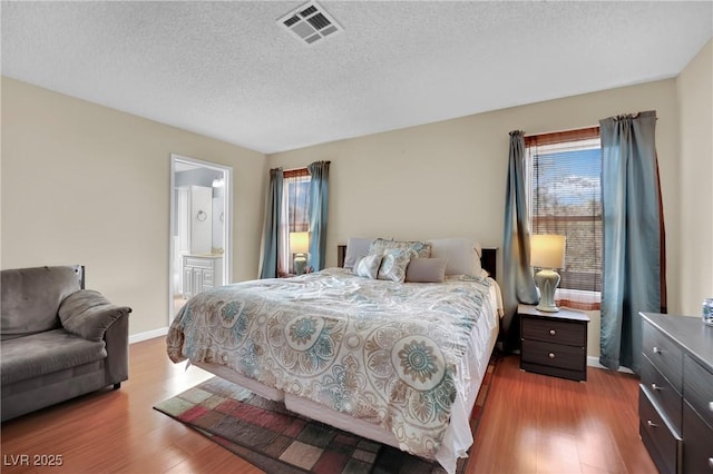 bedroom featuring visible vents, a textured ceiling, baseboards, and wood finished floors