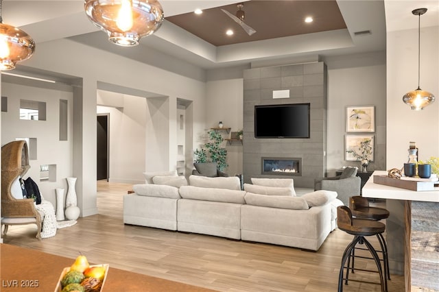 living room featuring a raised ceiling, a tile fireplace, and light hardwood / wood-style flooring