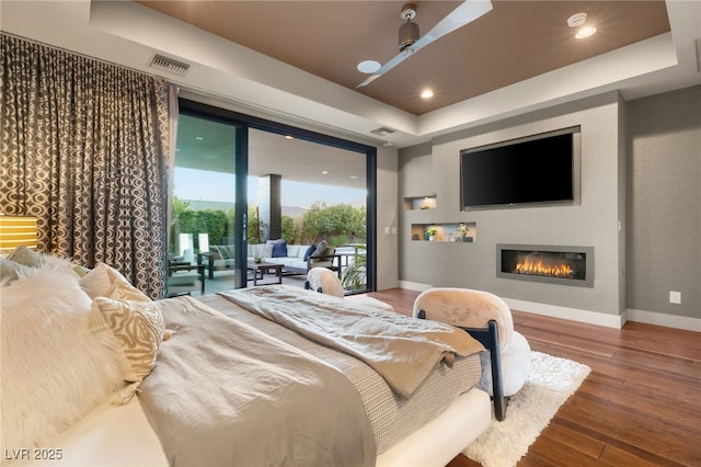 bedroom with hardwood / wood-style floors, access to exterior, and a tray ceiling