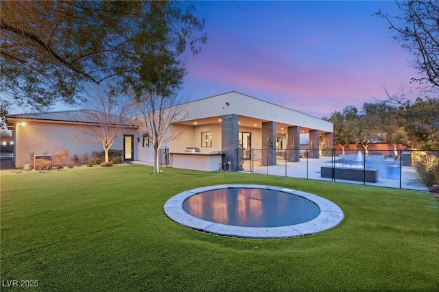 back house at dusk featuring a lawn