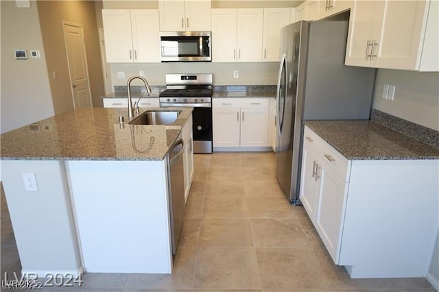 kitchen with sink, appliances with stainless steel finishes, white cabinets, a center island with sink, and dark stone counters