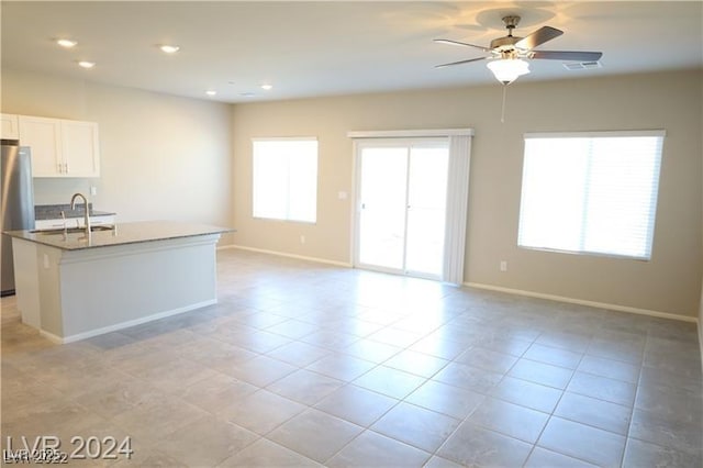 kitchen with dark stone countertops, white cabinets, a kitchen island with sink, light tile patterned floors, and ceiling fan