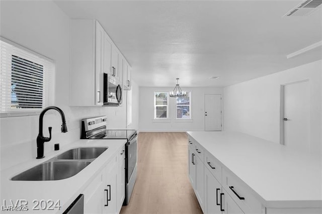 kitchen featuring appliances with stainless steel finishes, pendant lighting, sink, white cabinets, and light hardwood / wood-style flooring