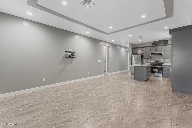 kitchen featuring gray cabinetry, stainless steel appliances, a center island, decorative light fixtures, and a raised ceiling