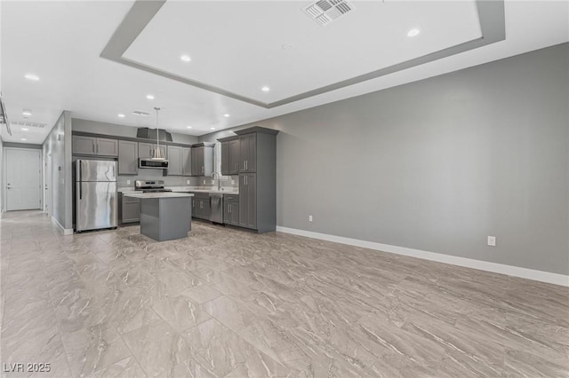 kitchen with a tray ceiling, a kitchen island, gray cabinets, and appliances with stainless steel finishes