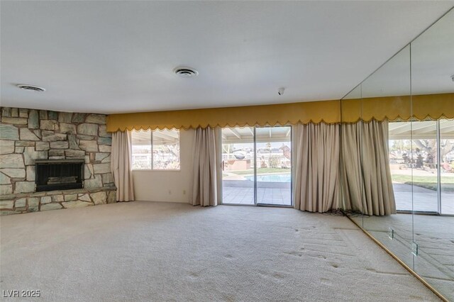 unfurnished living room featuring carpet floors, a stone fireplace, and visible vents