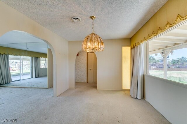 spare room with light carpet, an inviting chandelier, arched walkways, and a textured ceiling