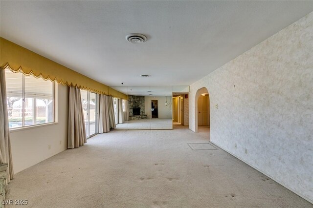 empty room with arched walkways, a stone fireplace, light carpet, and visible vents