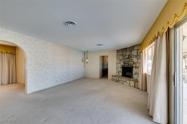 unfurnished living room with light carpet, visible vents, arched walkways, and a stone fireplace