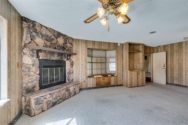 unfurnished living room with light carpet, a fireplace, wooden walls, and a textured ceiling