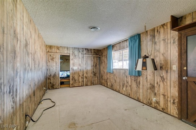 spare room with wood walls, visible vents, a textured ceiling, and light colored carpet