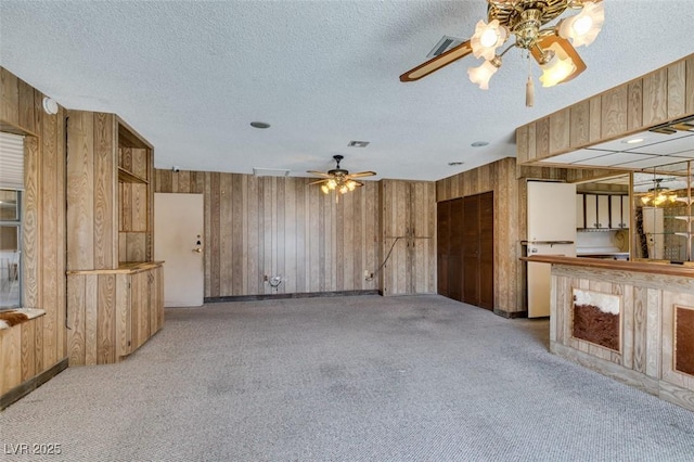 interior space featuring light carpet, visible vents, a ceiling fan, a textured ceiling, and wood walls