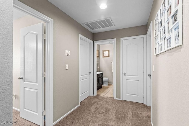 hallway with carpet floors, visible vents, and baseboards