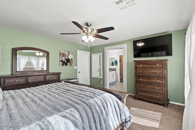 bedroom with ceiling fan, light colored carpet, visible vents, baseboards, and ensuite bath