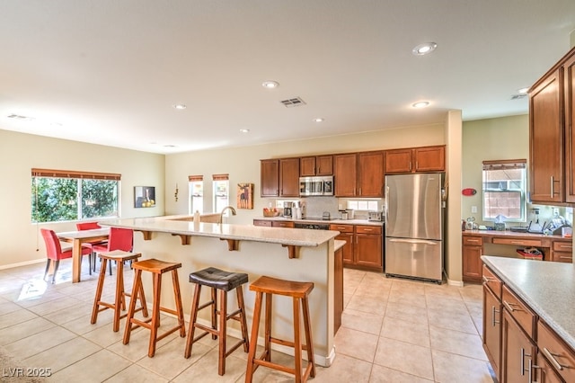 kitchen featuring an island with sink, appliances with stainless steel finishes, a breakfast bar, and plenty of natural light