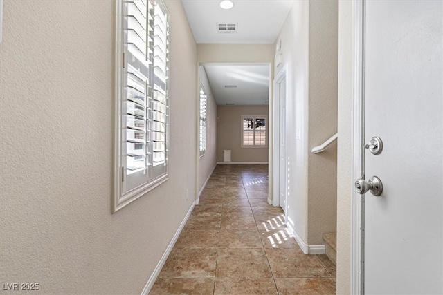 hall with light tile patterned floors, a textured wall, visible vents, and baseboards