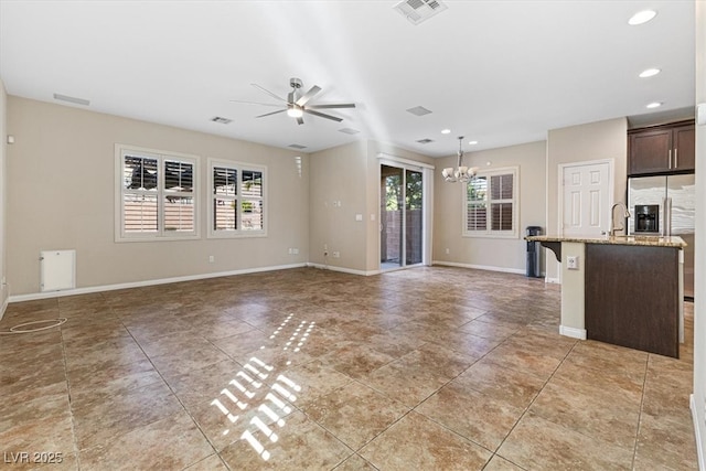 unfurnished living room with visible vents, plenty of natural light, baseboards, and ceiling fan with notable chandelier