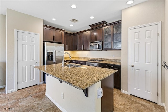 kitchen with light stone counters, appliances with stainless steel finishes, dark brown cabinets, a kitchen bar, and a sink