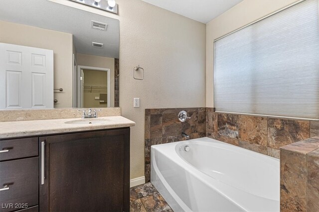 bathroom with visible vents, a garden tub, vanity, and baseboards